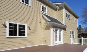 Composite deck in house backyard. Brown boards, white railing posts and veranda. Large, spacious, new construction.